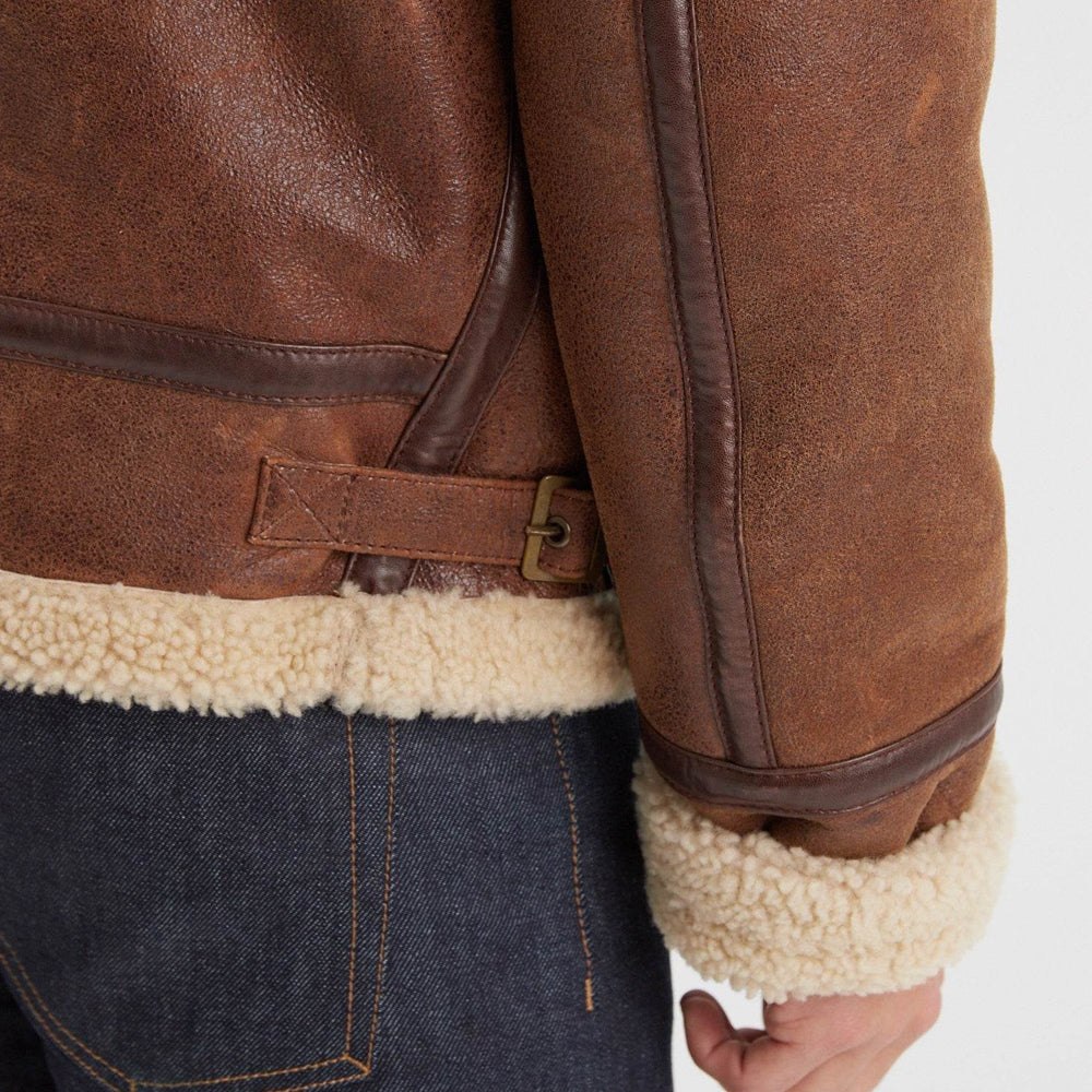 Vintage brown B-3 aviator jacket detail with adjustable side-waist buckle, bound sleeve seam, and exposed cream shearling