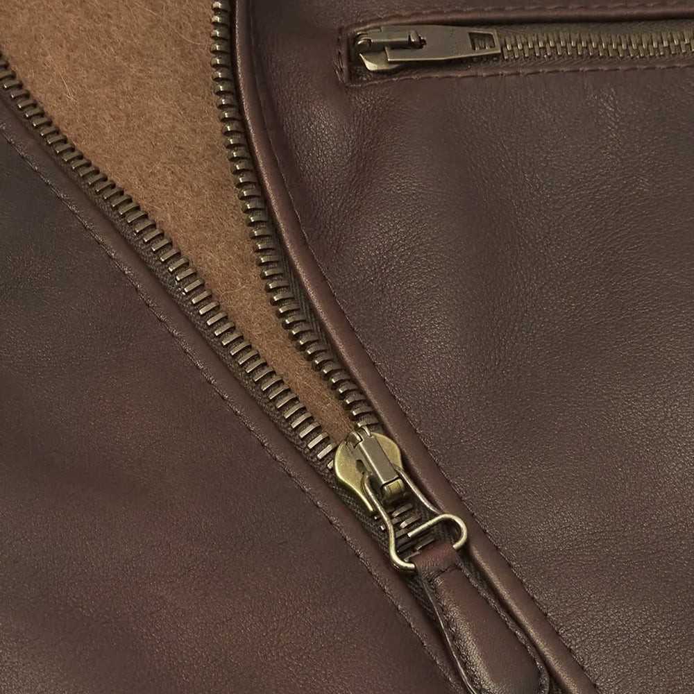 Close detail of the antique-brass YKK front zipper, chest pocket hardware and smooth waxed brown lambskin grain