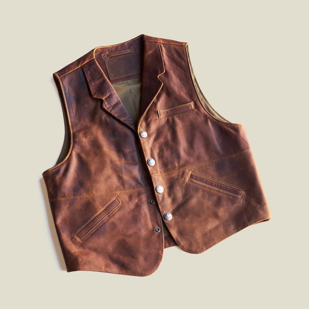 Angled flat-lay view of whiskey-brown concealed-carry leather waistcoat with pull-up shading and three exterior pockets