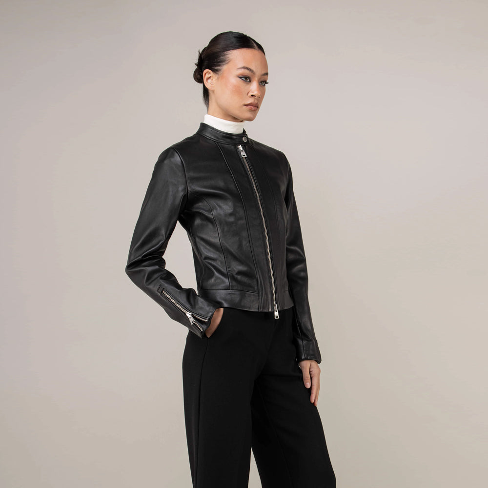 Three-quarter view of women’s black moto jacket showing a lower welt pocket and tailored waist