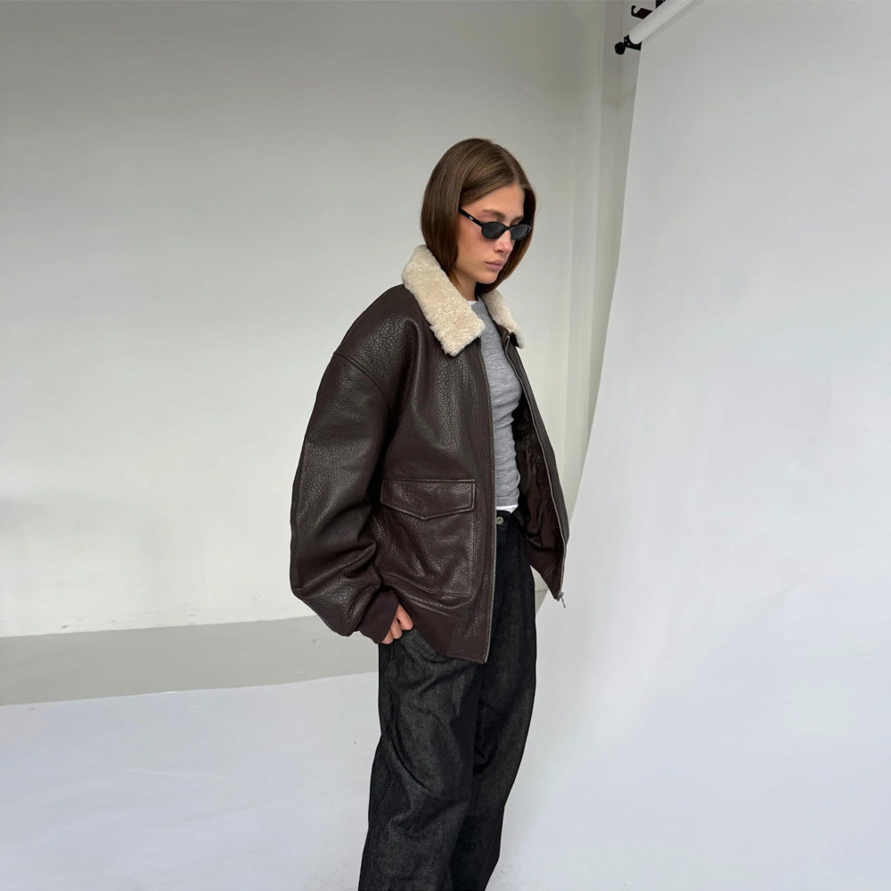 Three-quarter studio view of woman wearing a dark brown cow leather bomber jacket with open front