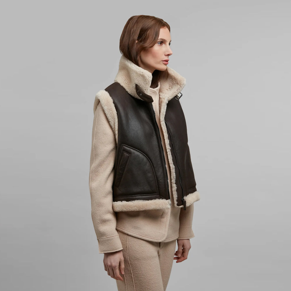 Woman wearing a dark brown shearling vest with an ivory stand collar over a cream knit outfit