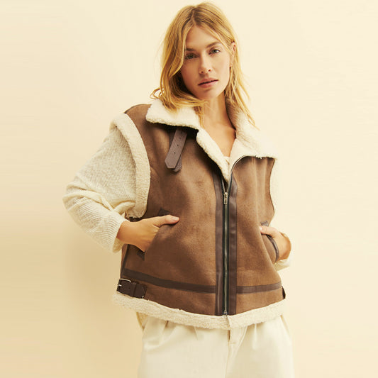 Woman wearing a brown suede aviator vest with cream faux-shearling trim, buckle collar and zip front.