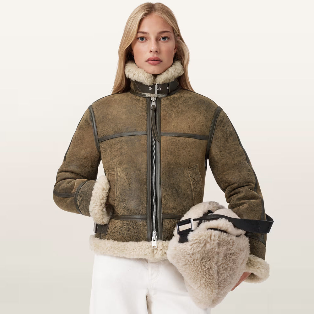 Front view of model wearing women's olive distressed B3 shearling aviator jacket with white trousers.
