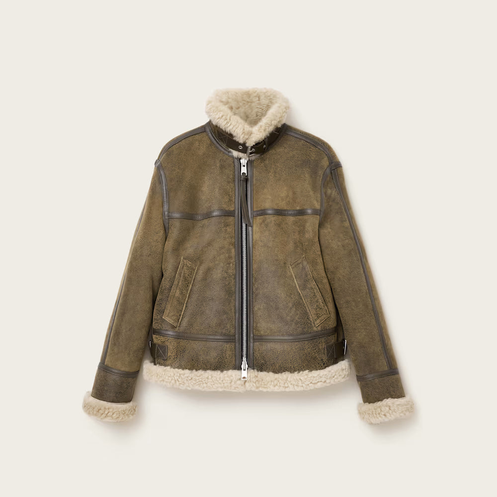 Flat lay product shot of women's olive distressed sheepskin shearling flight jacket on neutral backdrop.