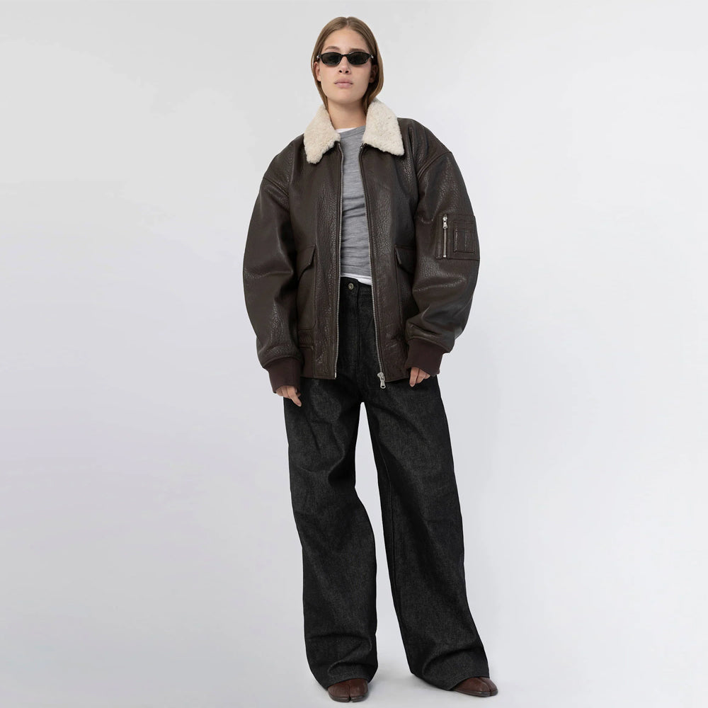 Full-length front view of woman in an oversized brown leather bomber jacket with ribbed cuffs and hem