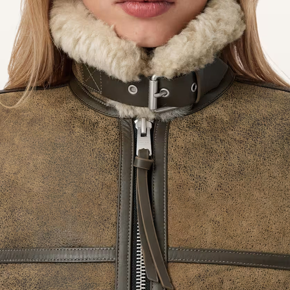 Close-up detail of high stand shearling collar with dark leather throat latch and silver metal buckle.