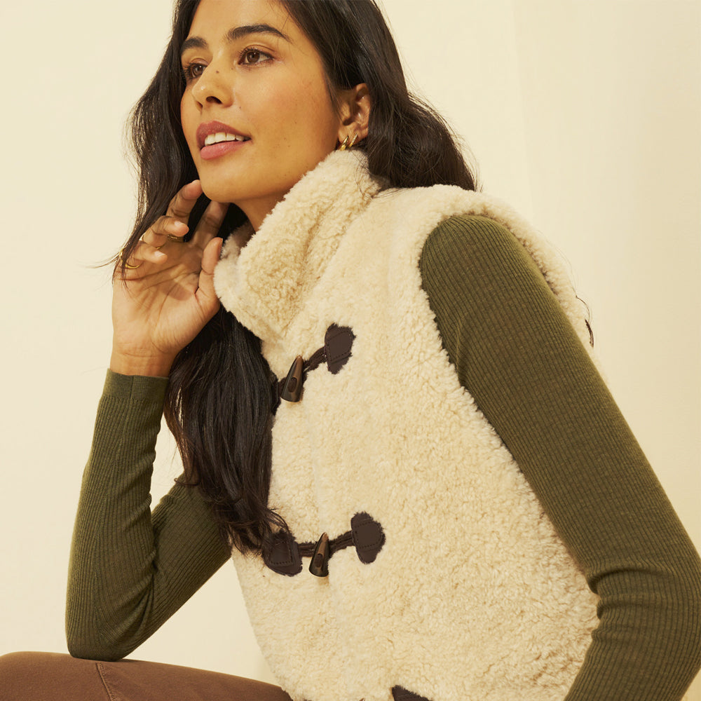 Side view of a women’s cream teddy fleece vest with softly finished armholes and a high collar.