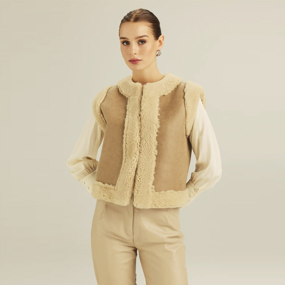 Woman wearing a tan reversible shearling vest with ivory trim over a cream blouse, front view