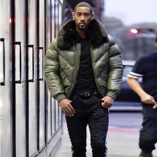 Front view of a model standing outside in the city wearing the men's olive green lambskin leather V-bomber jacket with hands in pockets.
