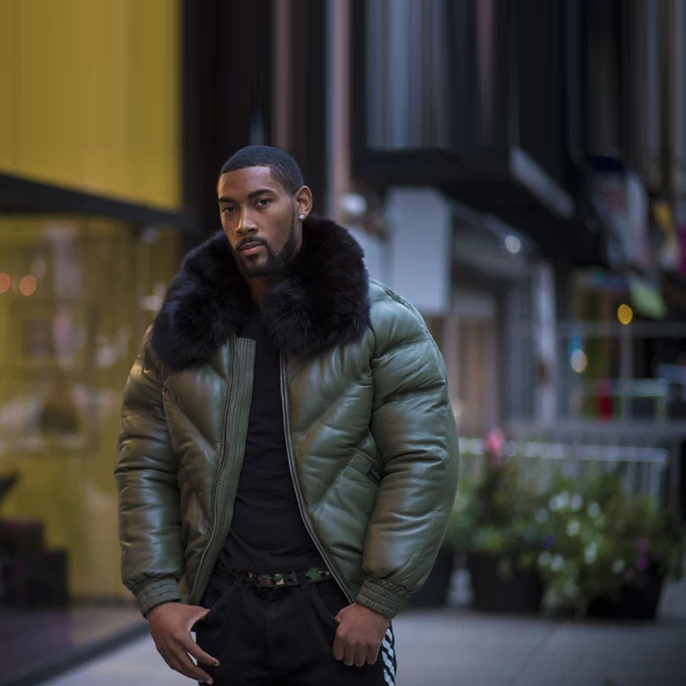 A model standing in the street, wearing the military olive-green lambskin leather V-bomber jacket, styled open with the front unzipped.