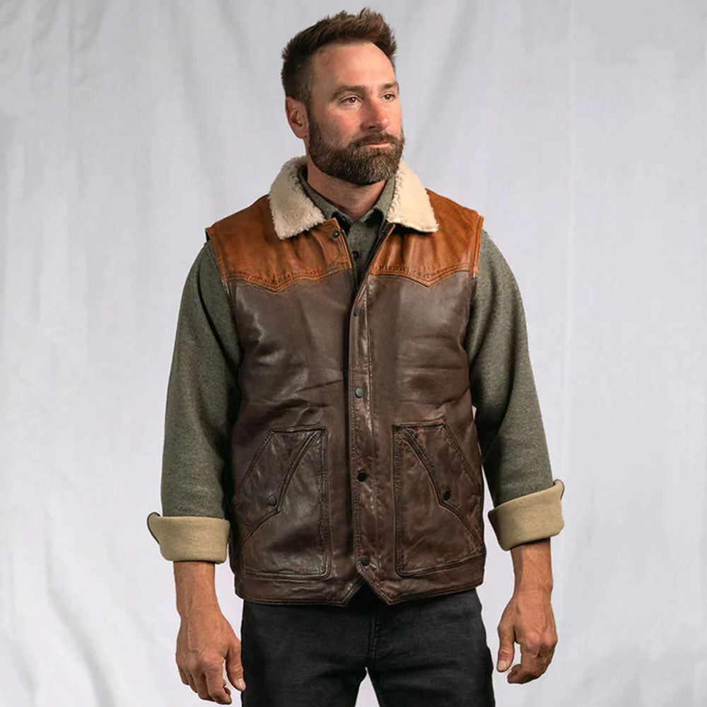 Lifestyle view of a man wearing the tobacco brown nappa shearling vest styled over a blue denim shirt.
